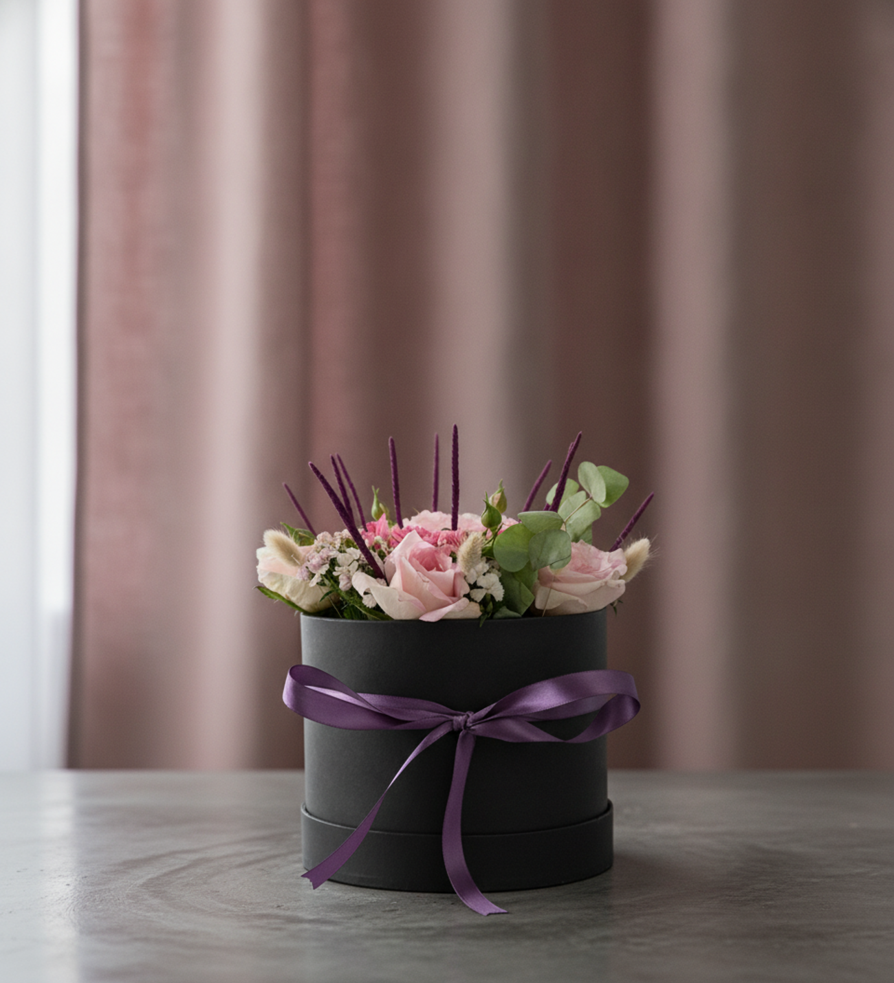 Rosa Rosen & Freesien in Schwarzer Box, Rosa Gartenrosen mit duftenden Freesien, Eukalyptus, Hasenschwanzgras und weichem strukturiertem Beiwerk, präsentiert in einer eleganten schwarzen Zylinderbox mit lila Schleife.