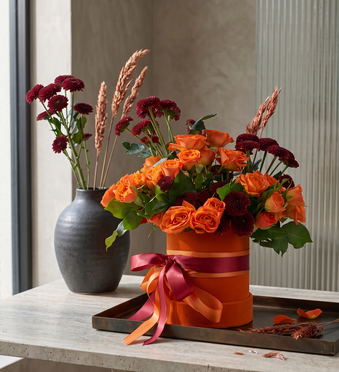 Roses Orange & Chrysanthèmes Bordeaux dans un Coffret, Des roses de jardin orange avec vingt chrysanthèmes boules bordeaux, de l'herbe de pampa et du gypsophile, finis de rubans orange et bordeaux dans un coffret en velours.