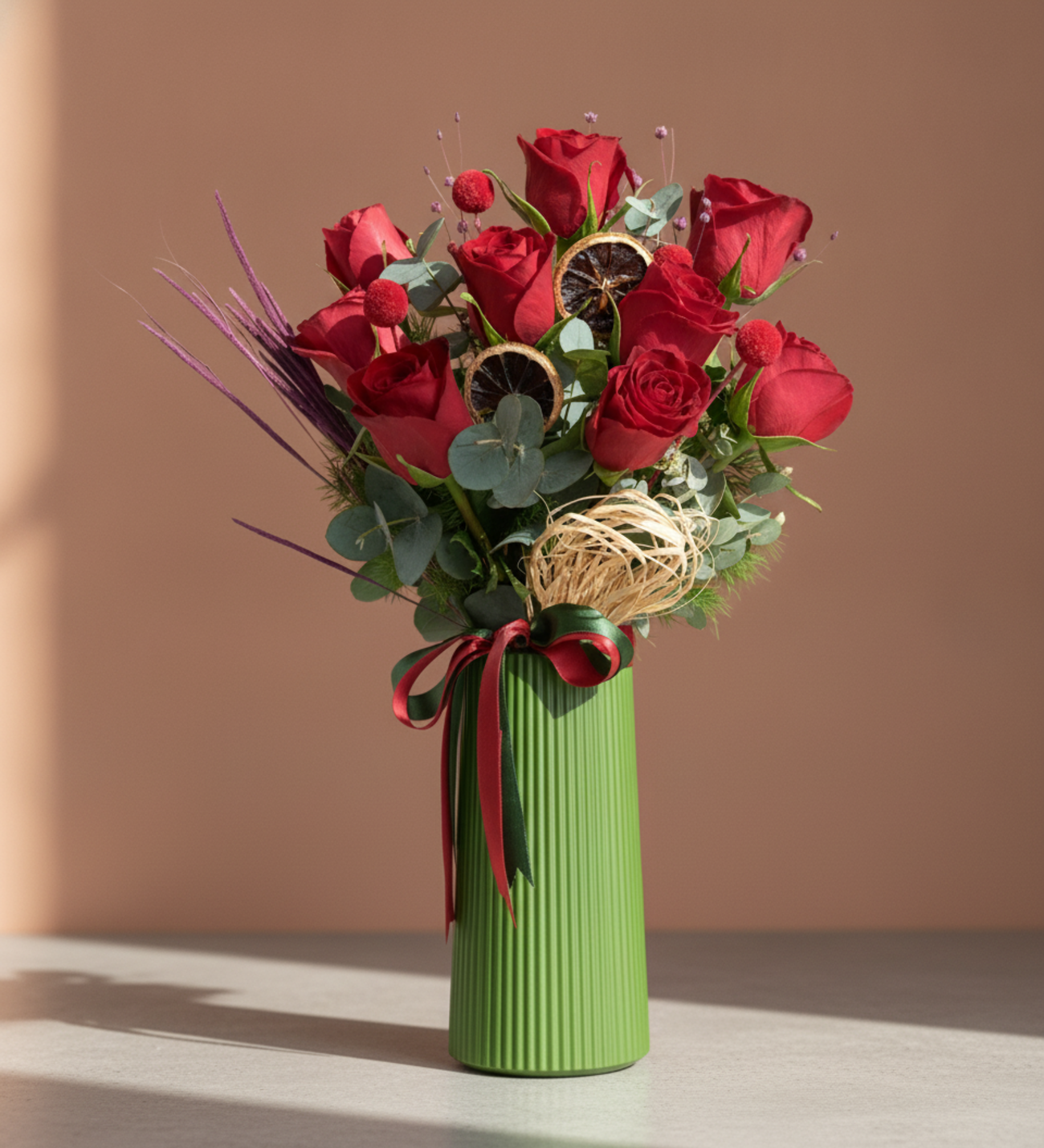 9 Rote Rosen in Gestreifter Bändervase, Neun rote Rosen in einer grün gestreiften Polymervase mit roten und dunkelgrünen Schleifen, Eukalyptus und getrockneten Akzenten, 20 cm hoch.