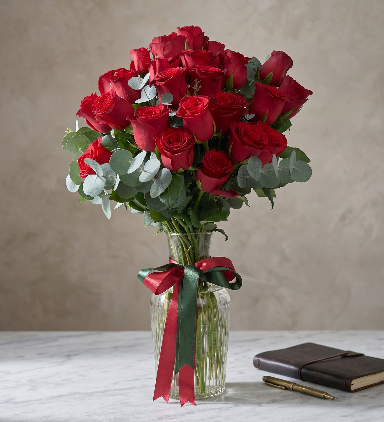 25 Rote Rosen in Gestreifter Glaskaraffenvase, Fünfundzwanzig rote Rosen in einer gestreiften Glaskaraffenvase mit dunkelgrünen und roten Schleifen sowie frischem Eukalyptus, etwa 30 bis 40 cm hoch.