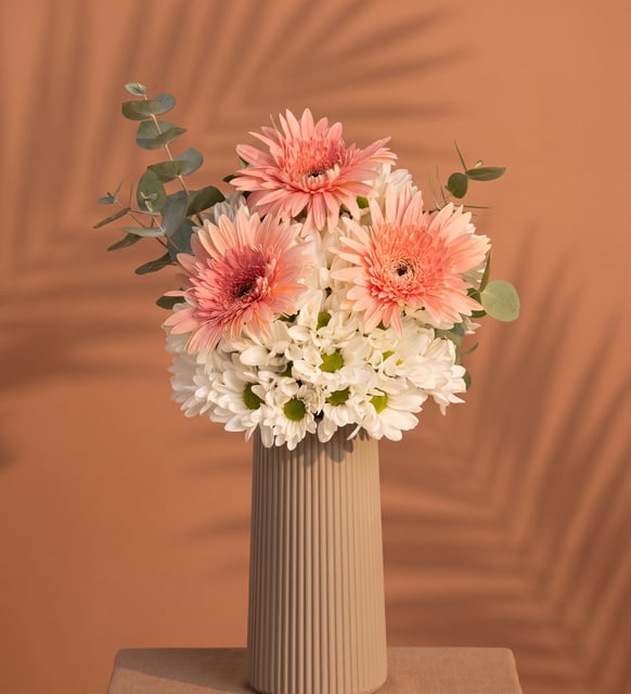 Marguerites Blanches et Gerberas Roses dans un Vase Beige Strié, Un joyeux mélange de marguerites blanches et de trois gerberas rose tendre avec de l'eucalyptus, dans un vase beige strié de 35 à 40 cm de haut.