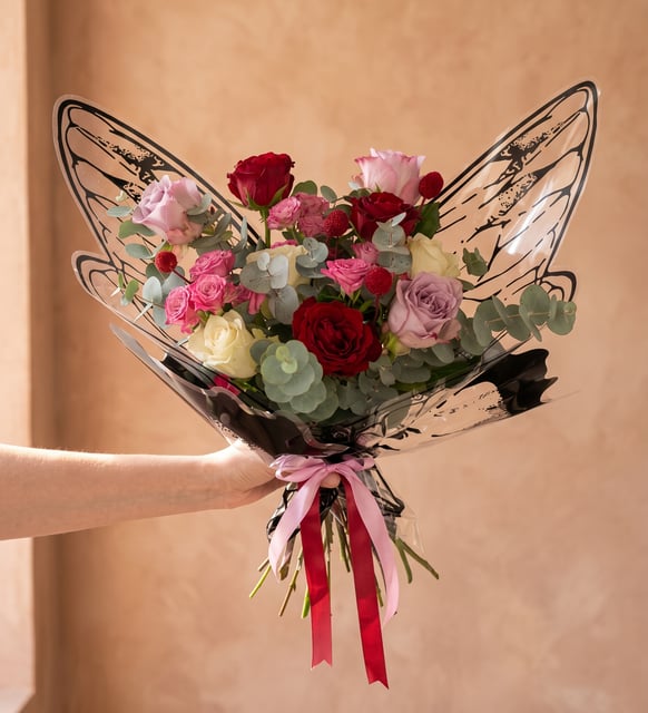 Roses Rouges, Lilas et Blanches en Bouquet Papillon, Trois roses rouges, trois lilas et trois blanches avec craspedia rouge et verdure, dans un emballage transparent en ailes de papillon avec rubans rouge et rose, de 40 à 50 cm.