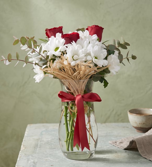 3 rote Rosen und weiße Margeriten in der Glasvase, Drei rote Rosen über einer Wolke aus weißen Margeriten und Eukalyptus in einer klaren Glasvase, mit rotem Band.