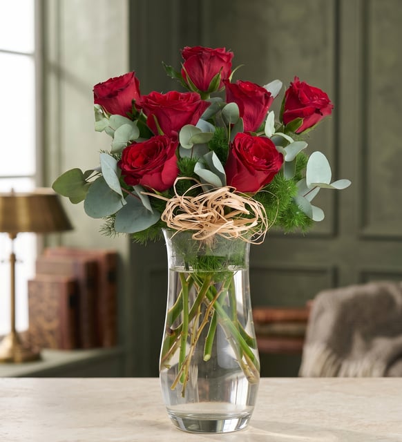 7 rote Rosen in einer Kristallglasvase, Sieben rote Rosen mit Eukalyptus und federleichtem Grün in einer hohen Kristallglasvase, mit Bastschleife.