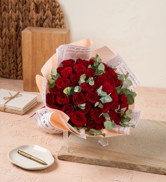 Strauß mit 50 roten Rosen, Fünfzig rote Rosen mit Eukalyptus in zartrosa Papier mit Zeitungsdruck, ein großer Strauß für eine Liebeserklärung.
