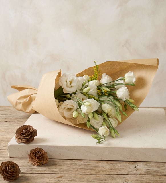 Bouquet de Lisianthus Blancs en Papier Kraft, Des lisianthus blancs tout en douceur, emballés dans un papier kraft naturel et noués d'un ruban jaune, d'une élégance discrète.